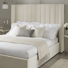 a bed with white linens and pillows in a neutral bedroom, next to a small side table