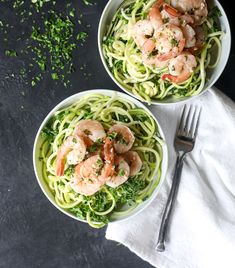 two bowls of shrimp and zucchini pasta on top of a white towel next to a fork