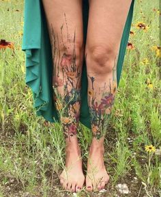 a woman's legs with tattoos on them and flowers all over her body in the grass