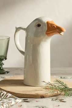 a white duck shaped mug sitting on top of a wooden board