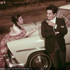 a man standing next to a woman in front of a car