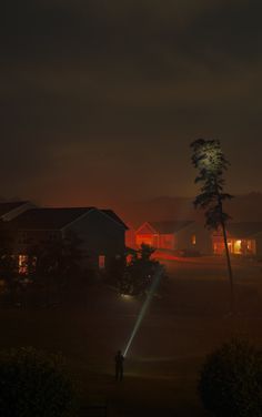 a person standing in the dark near some trees and buildings at night with lights on