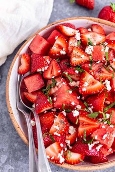 a bowl filled with sliced strawberries and topped with feta cheese on the side