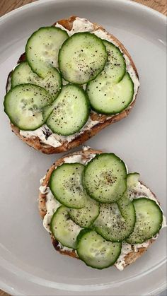 two pieces of bread with cucumbers on them sitting on a plate next to each other