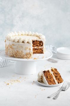 a slice of carrot cake with white frosting on a plate next to the rest of the cake