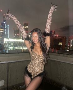 a woman posing on top of a roof with her arms in the air and wearing leopard print