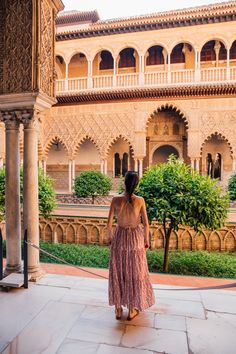 a woman standing in front of an ornate building with columns and arches, looking out into the distance