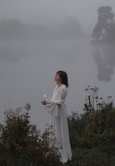 a woman standing on top of a hill next to a lake holding a lit candle