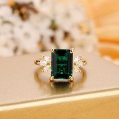 an emerald and diamond ring sitting on top of a gold box