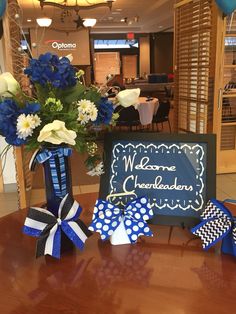 blue and white flowers are in a vase on a table with a welcome celebration sign