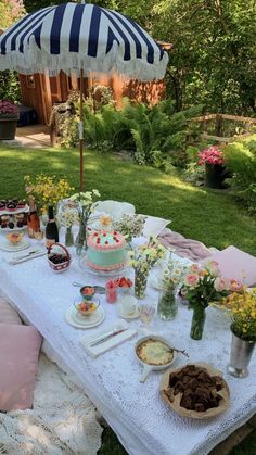 a table with cake and desserts on it in the grass near an open umbrella