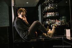 a man sitting in front of a bar talking on a cell phone while holding his foot up to his ear