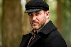 a man wearing a hat and jacket standing in the woods looking at the camera with an intense look on his face