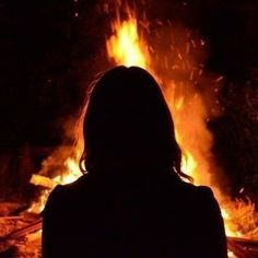 a woman standing in front of a fire with her back turned to the camera,