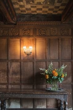 a vase with flowers sitting on top of a bench in front of a wooden paneled wall