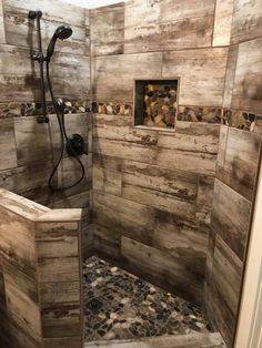 a walk in shower sitting next to a wooden wall and tiled floor with rocks on the ground