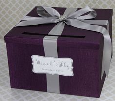 a purple box with a silver ribbon and a name tag on the front, sitting on a table