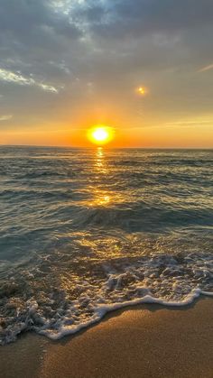 the sun is setting over the ocean with waves coming in to shore and sand on the beach