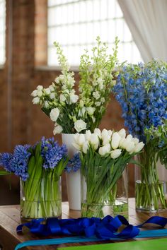 three vases filled with white and blue flowers on a wooden table next to ribbon