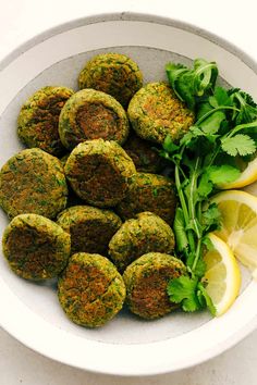 a white bowl filled with food next to lemon wedges and cilantro leaves