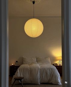 a white bed sitting under a light fixture in a bedroom next to a chair and table