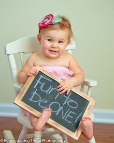 a baby sitting in a rocking chair holding a chalk board