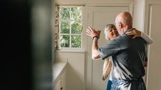 an older man and woman standing in front of a window taking pictures with their cell phones