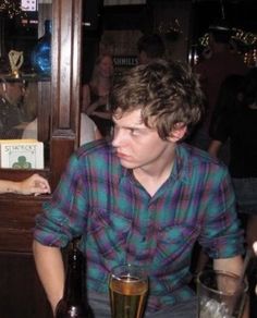 a young man sitting at a table with a glass of beer in front of him