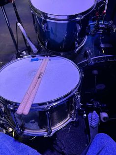 two drums are sitting next to each other in front of a drum set with sticks sticking out of it