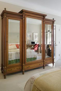 a large wooden armoire with mirrored doors in a bedroom next to a white bed