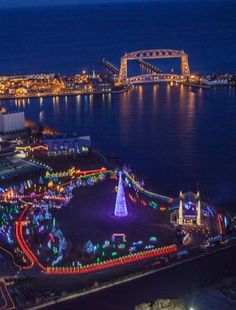 an aerial view of a fairground at night with lights on the ground and water in the background