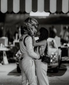 a man and woman kissing while standing next to each other in front of some cars