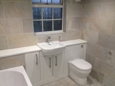 a white toilet sitting next to a bath tub under a window in a room with tile walls