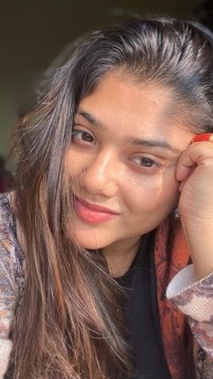 a woman with long hair is smiling and holding a cell phone to her ear while sitting down