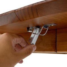 a hand is holding the door handle on a wooden shelf with two metal clips attached to it