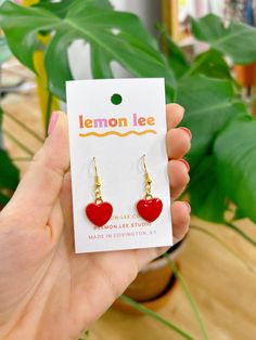 a person holding up a pair of heart shaped earrings in front of a potted plant