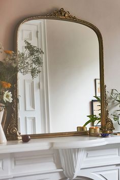 a mirror sitting on top of a mantle next to a vase with flowers in it