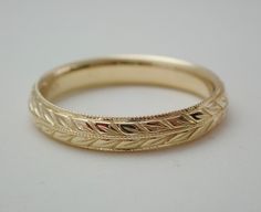 a gold wedding band that has been engraved with leaves on the inside and outside, sitting on a white surface