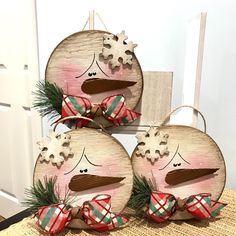 three wooden snowmen with bows on their heads are sitting in front of a door