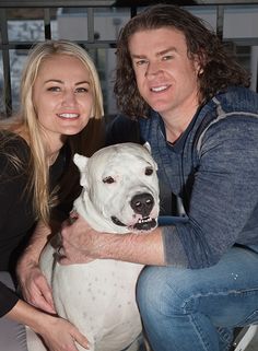 a man and woman pose for a photo with a large white dog in their lap