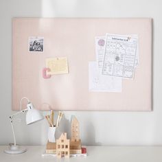 a white desk topped with a lamp next to a pink bulletin board