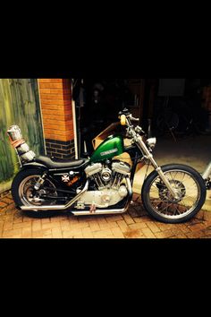 a green motorcycle parked in front of a brick building next to a sidewalk and door