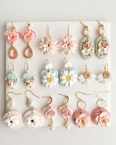 there are many different types of earrings on the white board with flowers and hearts hanging from them