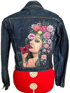 a jean jacket with a woman's face painted on the back and flowers in her hair