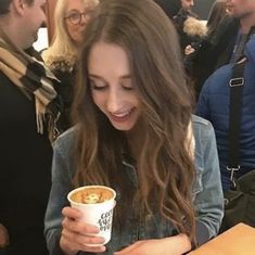 a girl is smiling and holding a cup of coffee in front of other people at an event