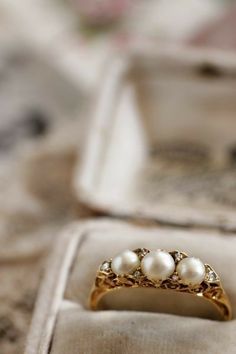 an old fashioned ring with three pearls on it sitting in a box next to some other items