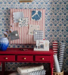 a red table topped with a blue vase filled with flowers next to a sewing machine