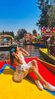 a woman sitting on the edge of a boat in a body of water with brightly colored boats behind her