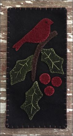 a red bird sitting on top of a black piece of felt next to leaves and berries