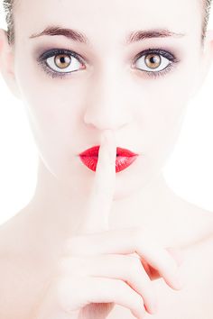 a woman making a hush with her finger to her lips while wearing red lipstick and black eyeliners